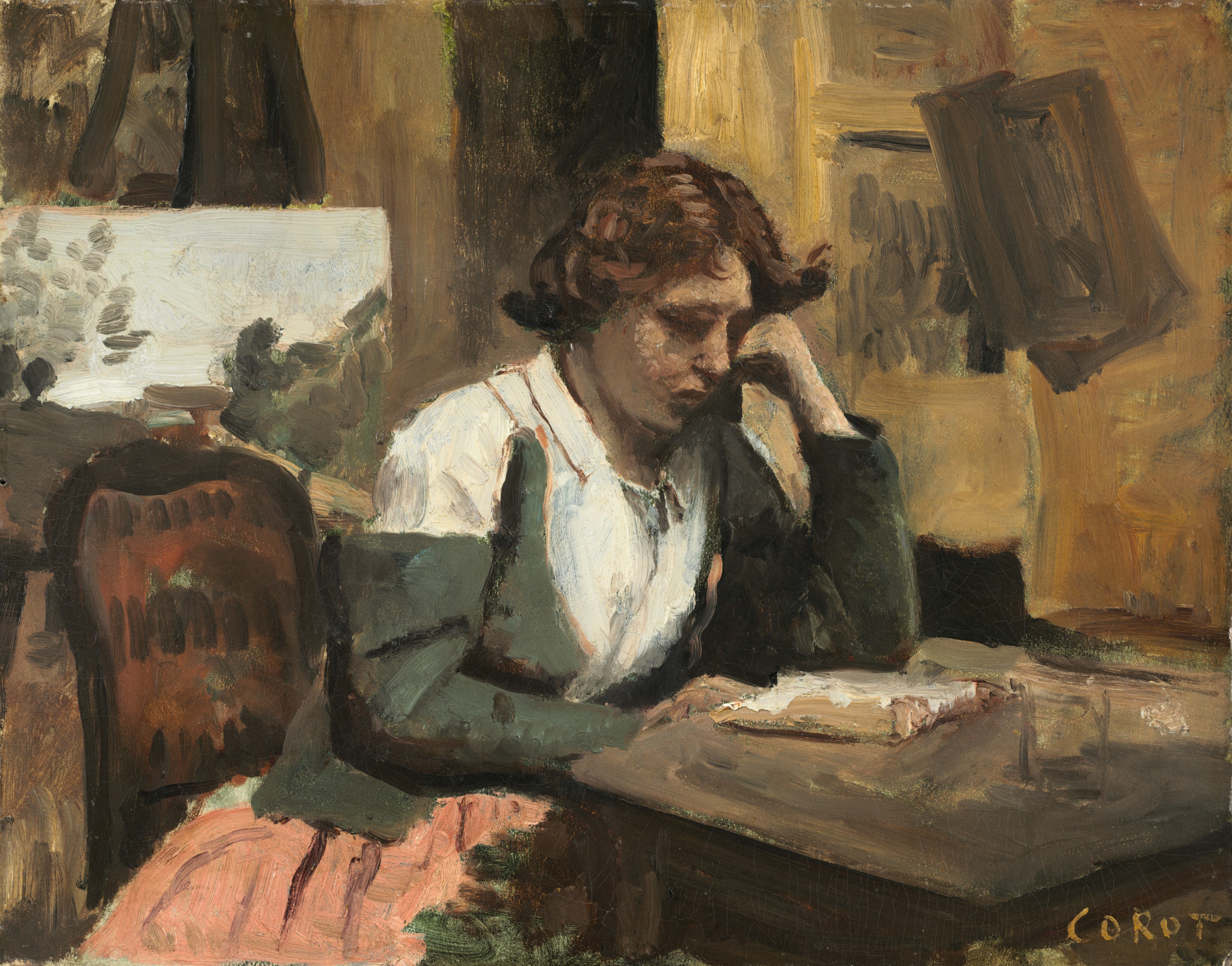 A woman seated at a table, absorbed in reading an open book in an artist's studio